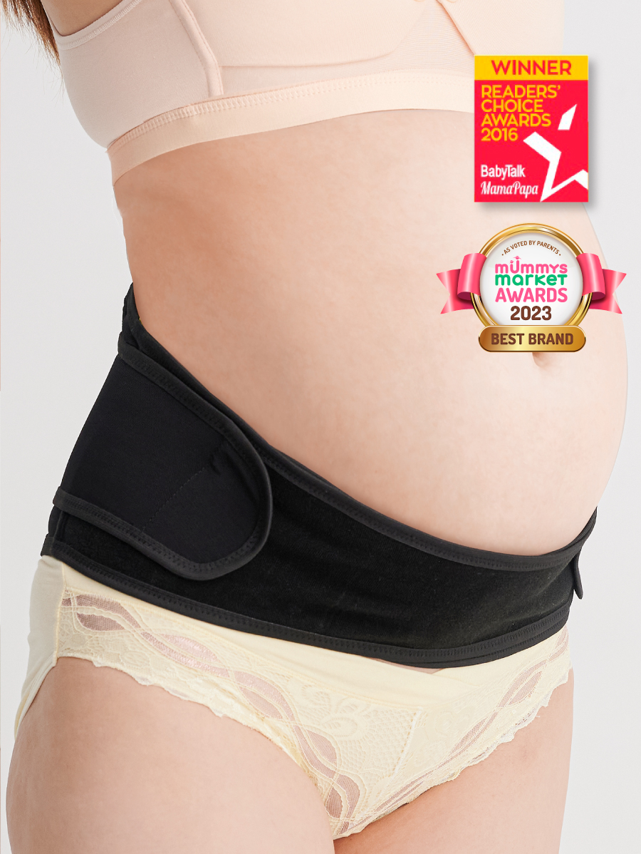 A pregnant woman wearing a beige bikini bottom and a black Bmama pregnancy support belt, which has a hook-and-loop closure and is positioned around the belly.